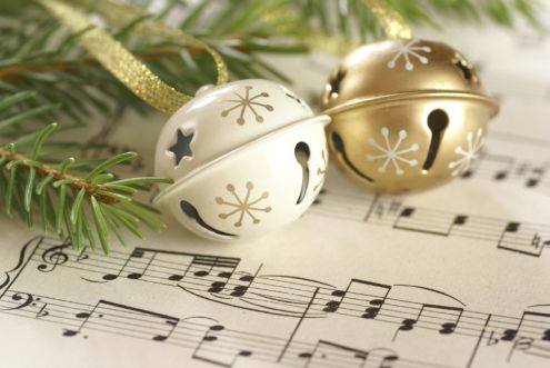 Valkoinen ja kullanvärinen kulkunen joululaulun nuottien päällä vierellä kuusenoksa.