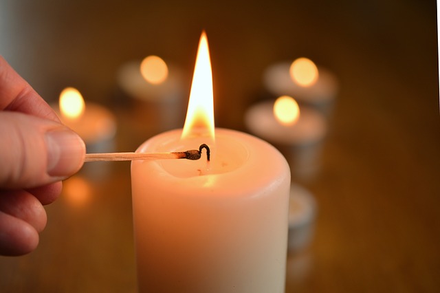 1. adventtisunnuntai messu Käsi sytyttää tulitikulla valkoista kynttilää. Taustalla näkyy himmeästi tuikkuja.